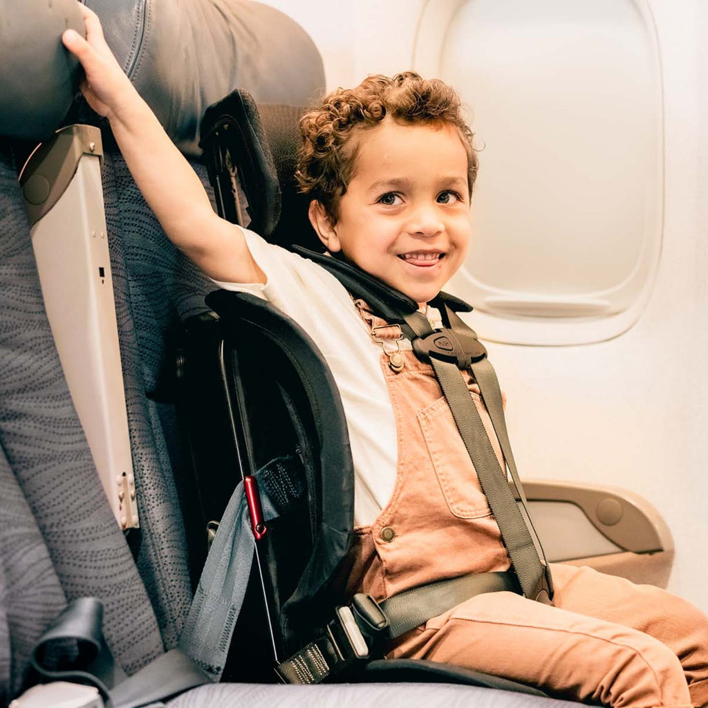 Child sitting in an airplane seat with a car seat